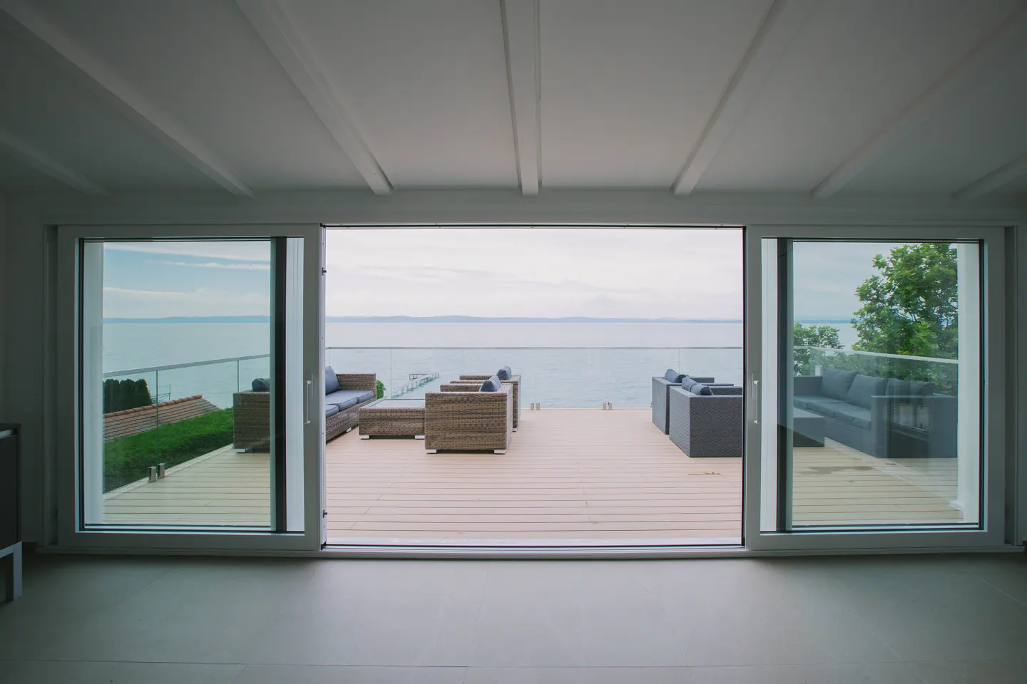 View from a bright room through sliding glass doors to a deck with outdoor furniture and a lake view.