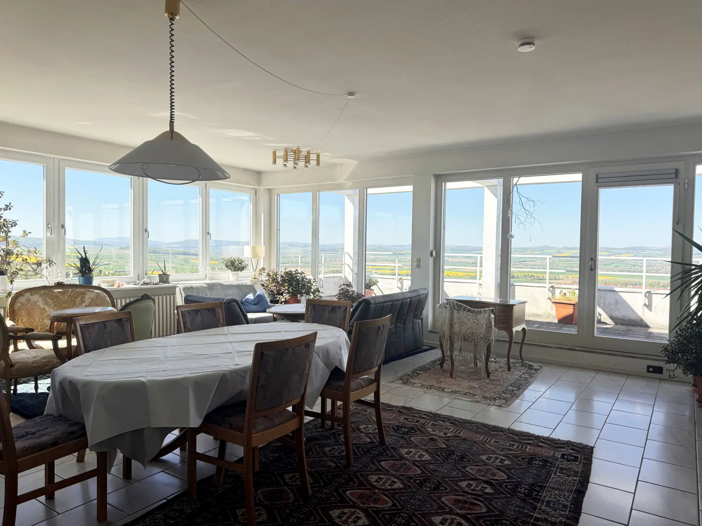 Bright, airy living room with a large dining table, chairs, and a view of green fields through large windows.
