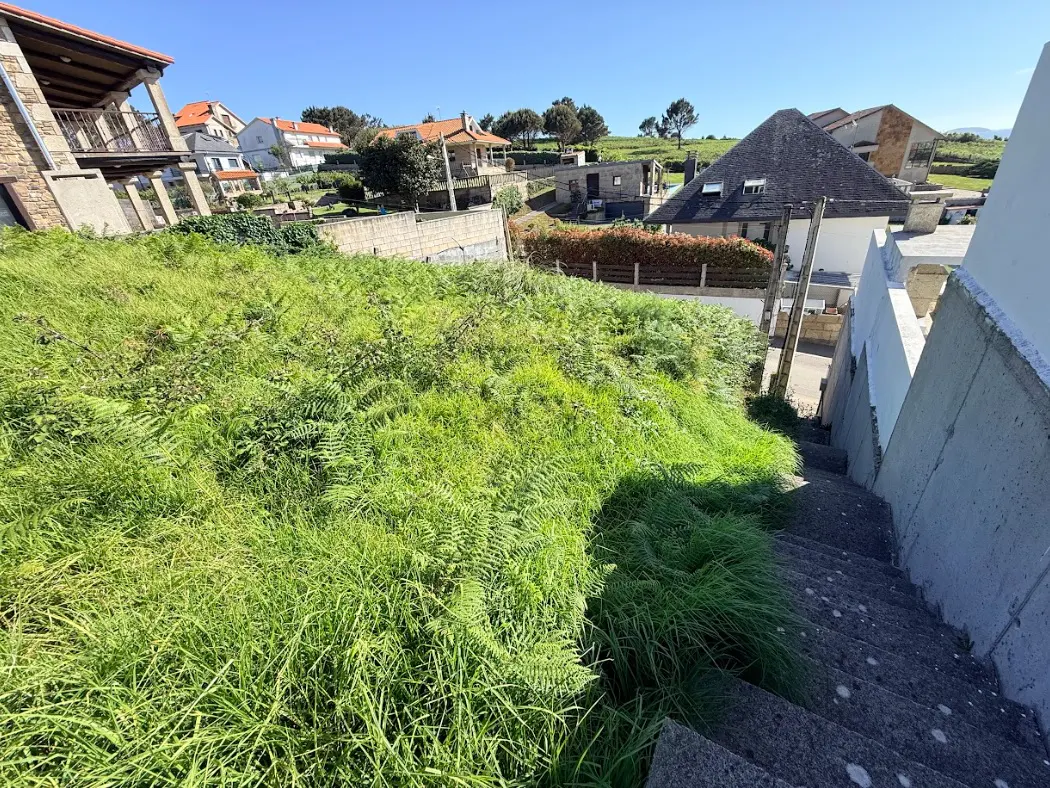 View of a grassy lot with concrete steps leading down, houses in the background under a blue sky.