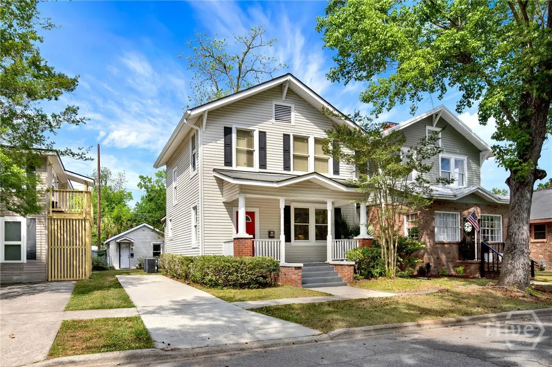 Two-story house with light gray siding, black shutters, and a red front door. A concrete driveway leads to a detached garage.
