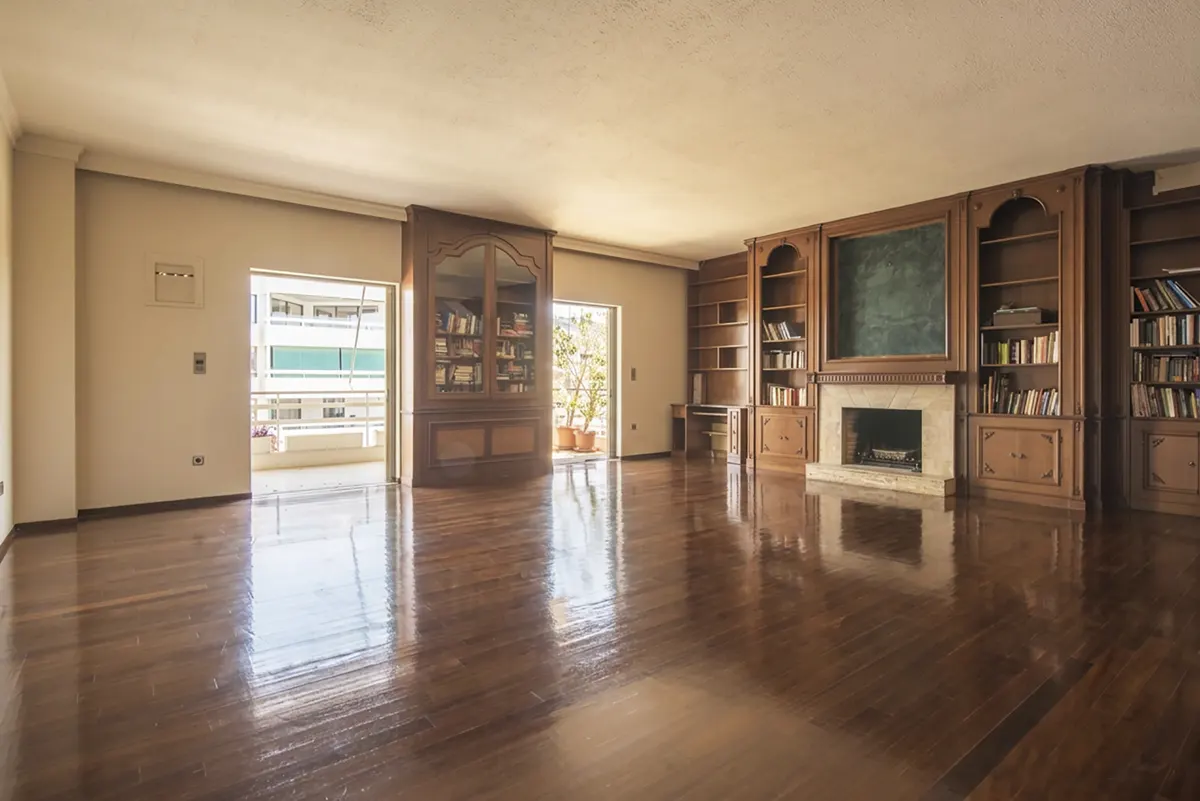 Spacious living room with hardwood floors, built-in wooden bookshelves, fireplace, and balcony access.