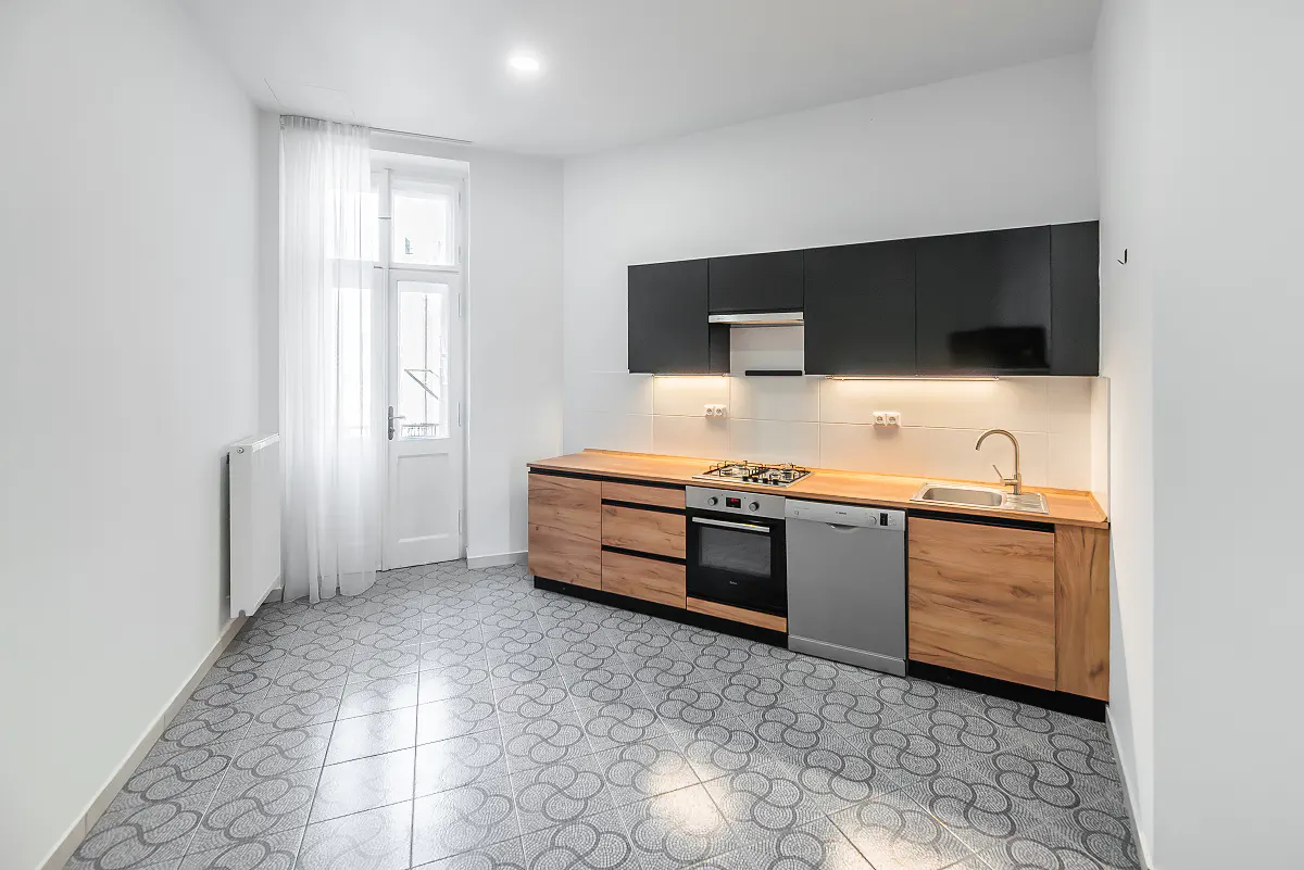 Bright kitchen with black cabinets, wood counters, and stainless steel appliances. Patterned tile floor and white walls.