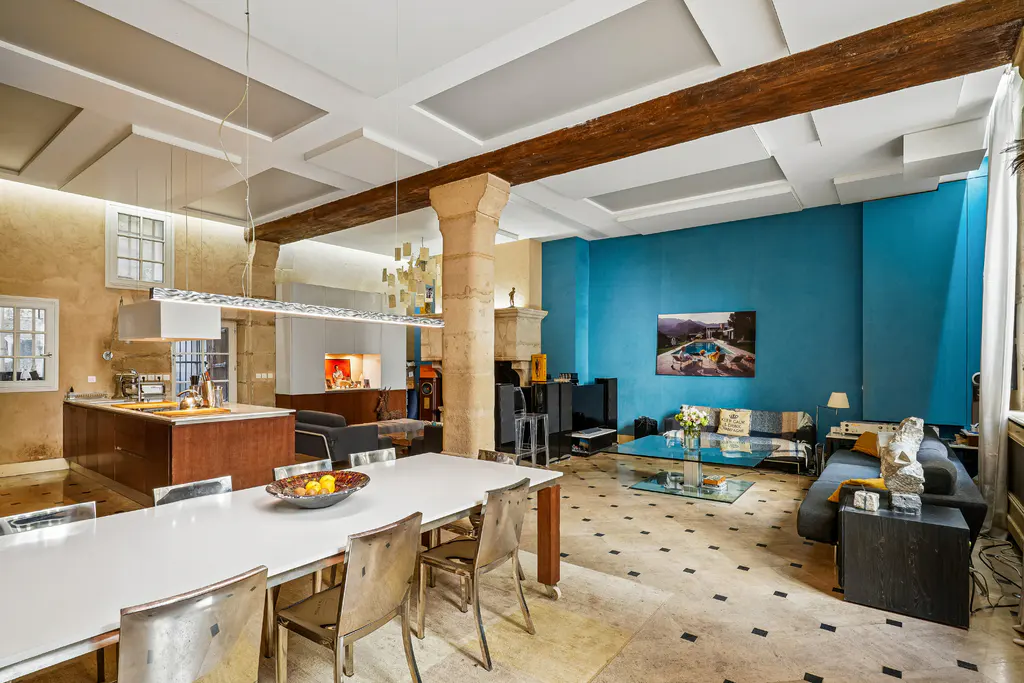 Open-concept living space with a white dining table, kitchen island, and blue accent wall with sofas and a glass coffee table.