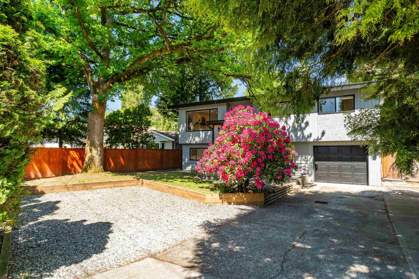 Exterior of a two-story gray house with a black garage door and a large pink rhododendron bush in the front yard.