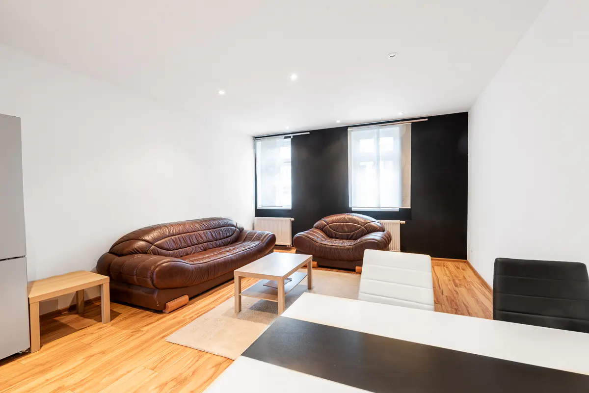 Living room with brown leather sofa and chair, light wood floors, and black accent wall with two windows.