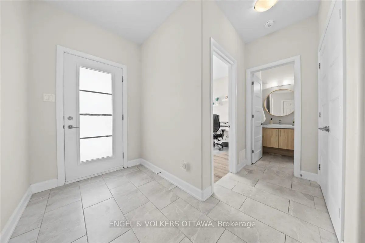 Bright hallway with gray tile floor, white walls, and three white doors leading to an office, bathroom, and closet.