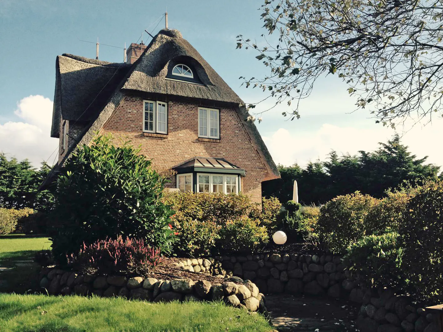 A brick house with a thatched roof surrounded by lush greenery.
