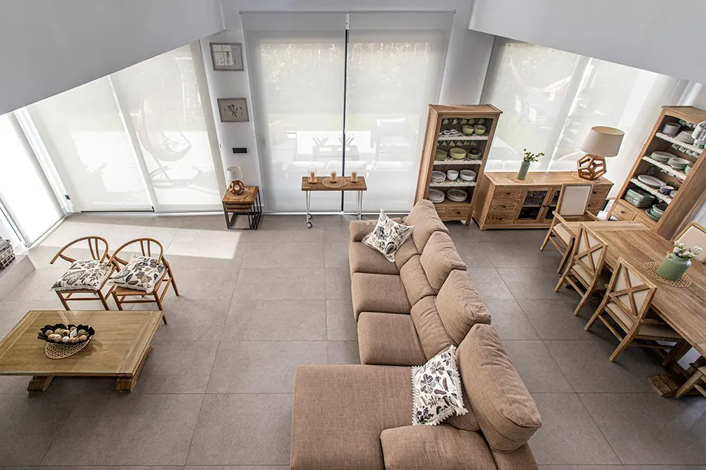Bright, modern living room with a brown sectional sofa, wooden dining table, and large windows with white blinds.