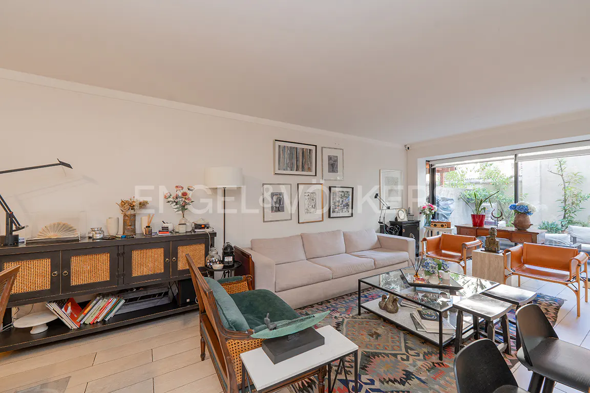 Living room with a beige sofa, glass coffee table, patterned rug, and a view of a garden through a large window.