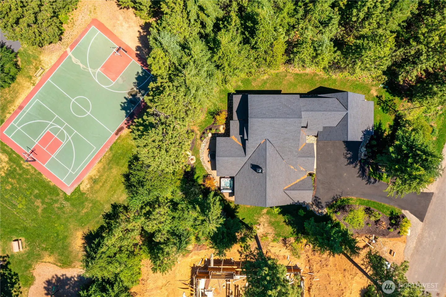 Aerial view of a house with a dark gray roof, surrounded by trees, and a basketball court with red and green paint.