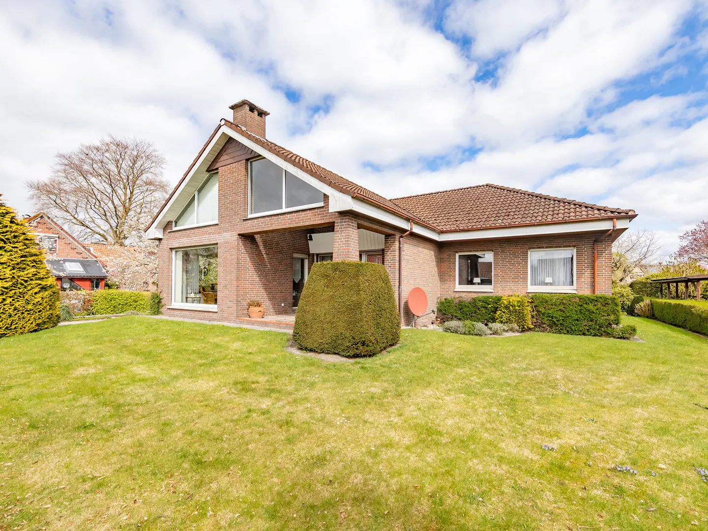 Exterior view of a brick house with a green lawn, trimmed hedges, and a cloudy sky.