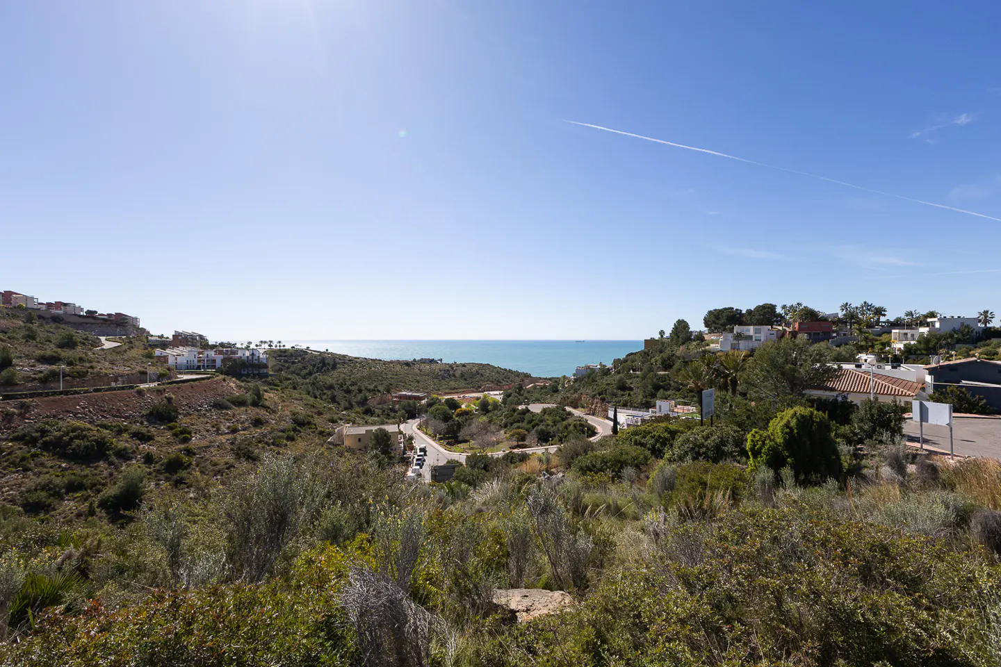 Scenic view of hillside homes overlooking the ocean under a clear blue sky with green vegetation.