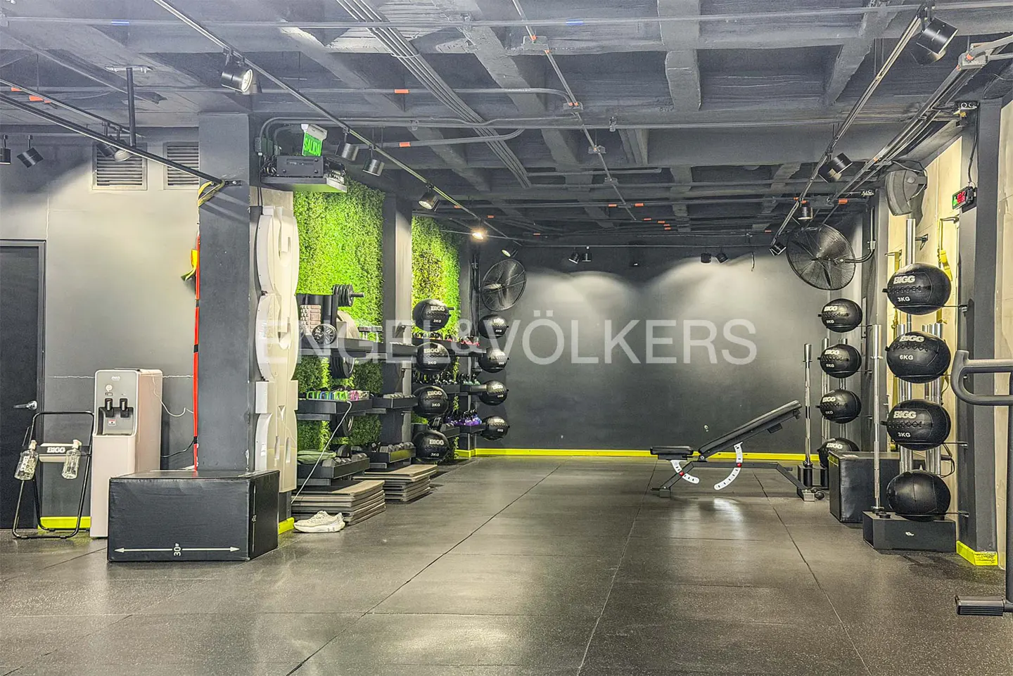 Gym interior with black floor, weights, and green moss wall. Engel & Völkers logo on the back wall.