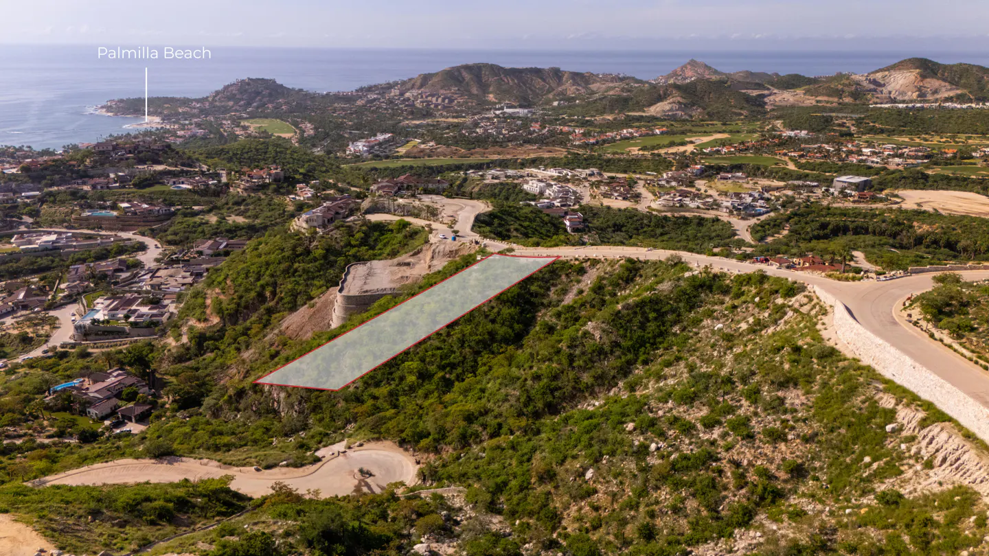 Aerial view of a vacant lot with a red border on a green hillside, with Palmilla Beach in the background.