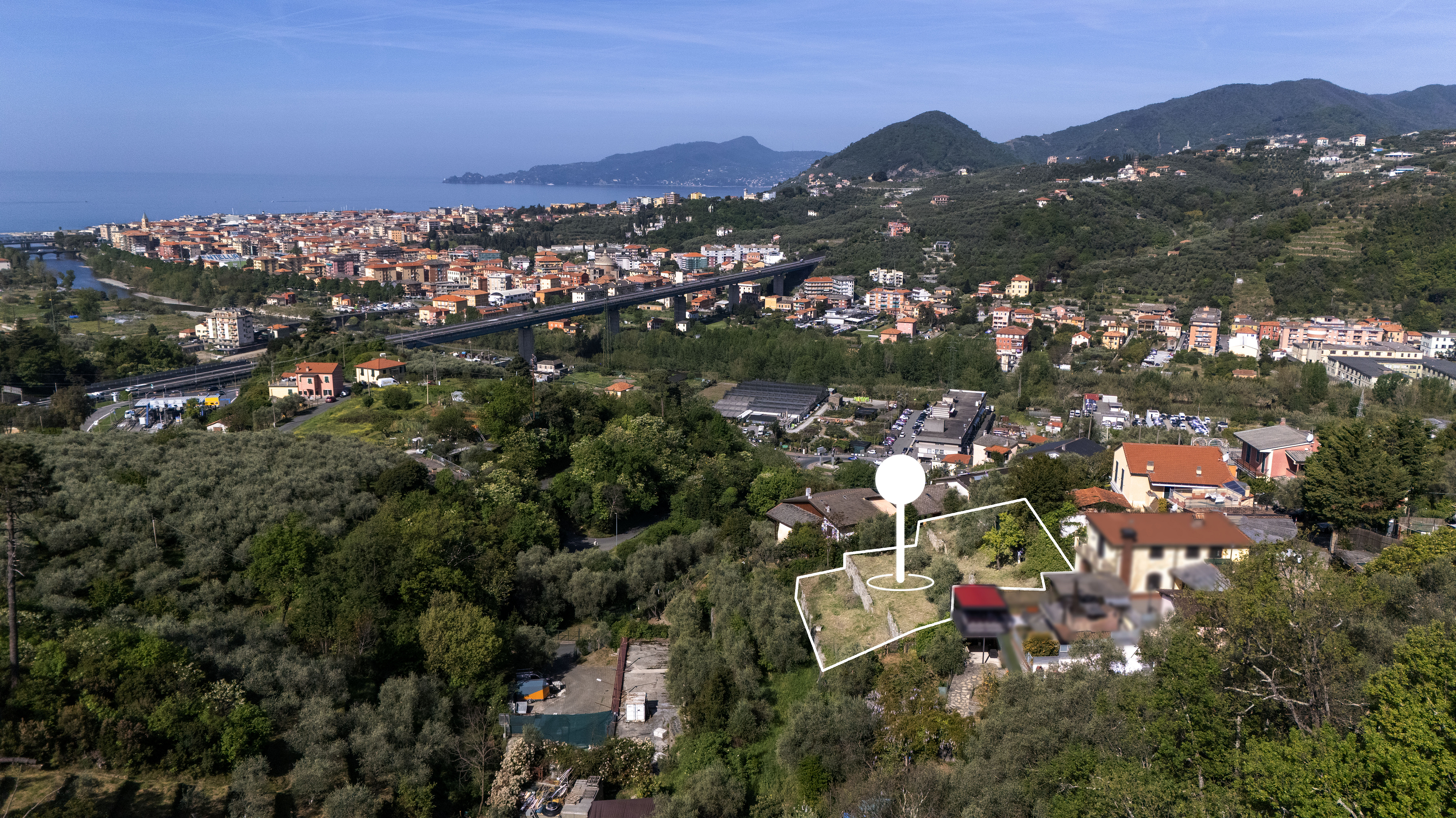 Aerial view of a property outlined in white, with a white pin marker, overlooking a city, mountains, and the sea.