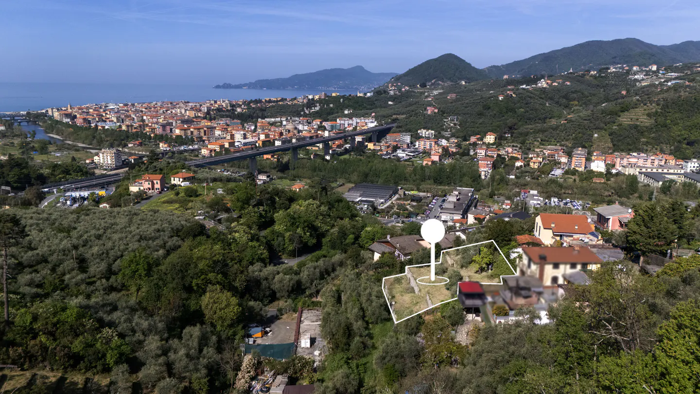 Aerial view of a property outlined in white, with a white pin marker, overlooking a city, mountains, and the sea.