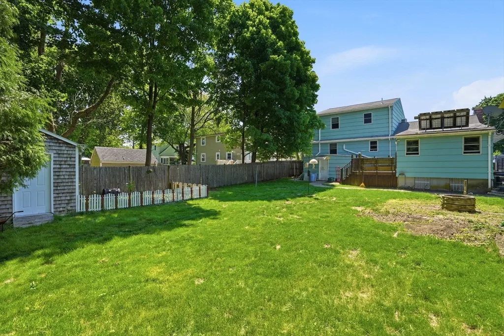 A large, green lawn with a light blue house, a shed, and a wooden fence in the background.