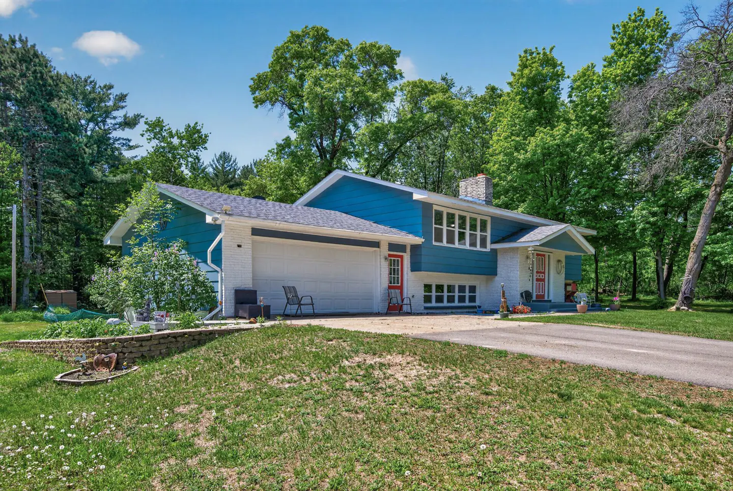 Exterior view of a blue and white house with a gray roof, red doors, and green trees in the background.