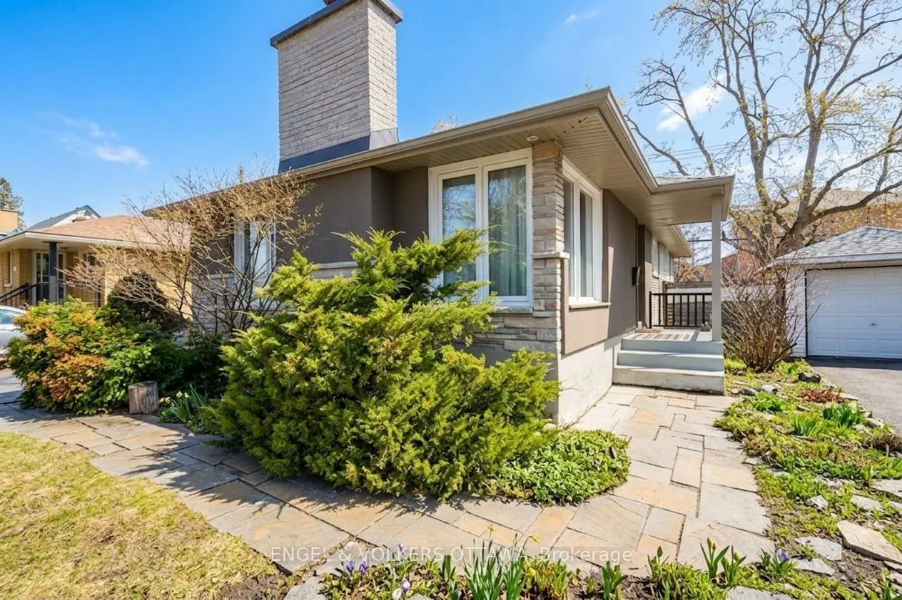 Exterior of a one-story house with a stone chimney, gray stucco, and a stone walkway leading to the front porch.