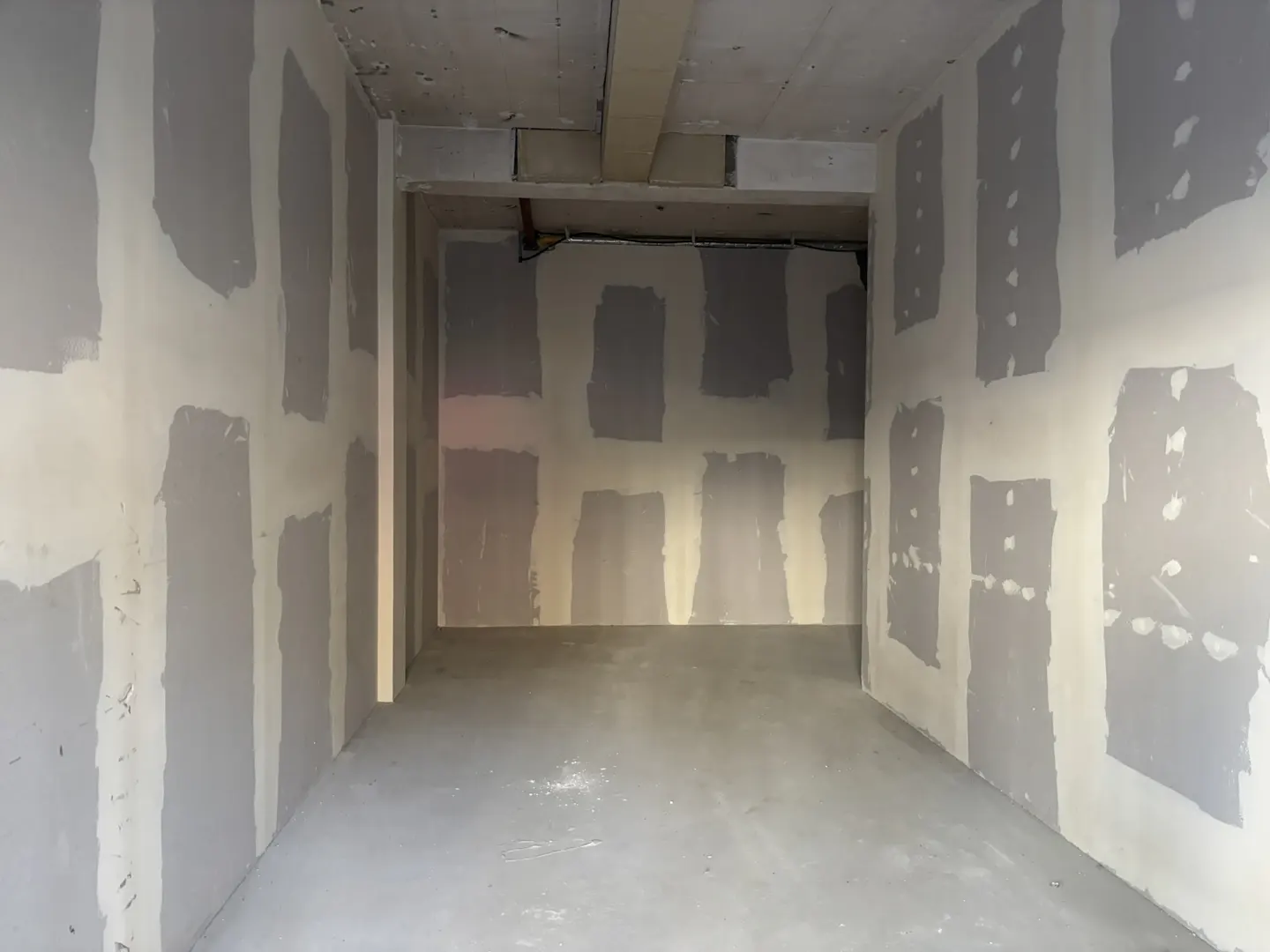Unfinished room with gray concrete floor and white walls covered in gray patches of drywall compound.