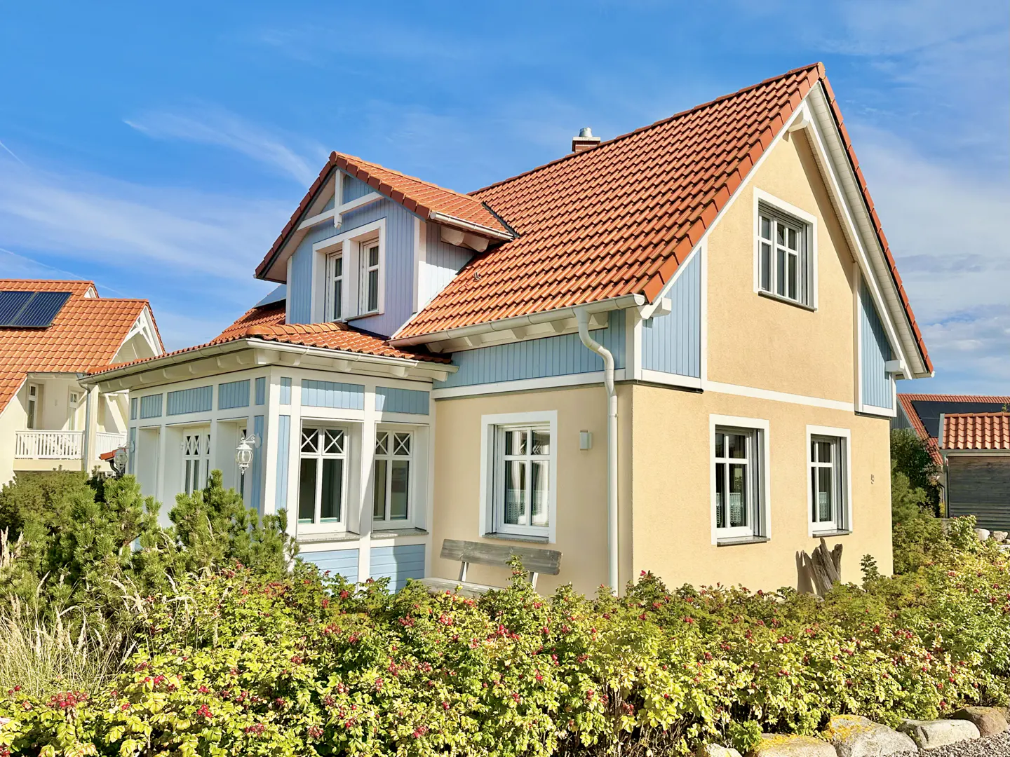 Two-story house with orange tile roof, blue and yellow siding, white trim, and green bushes in front.