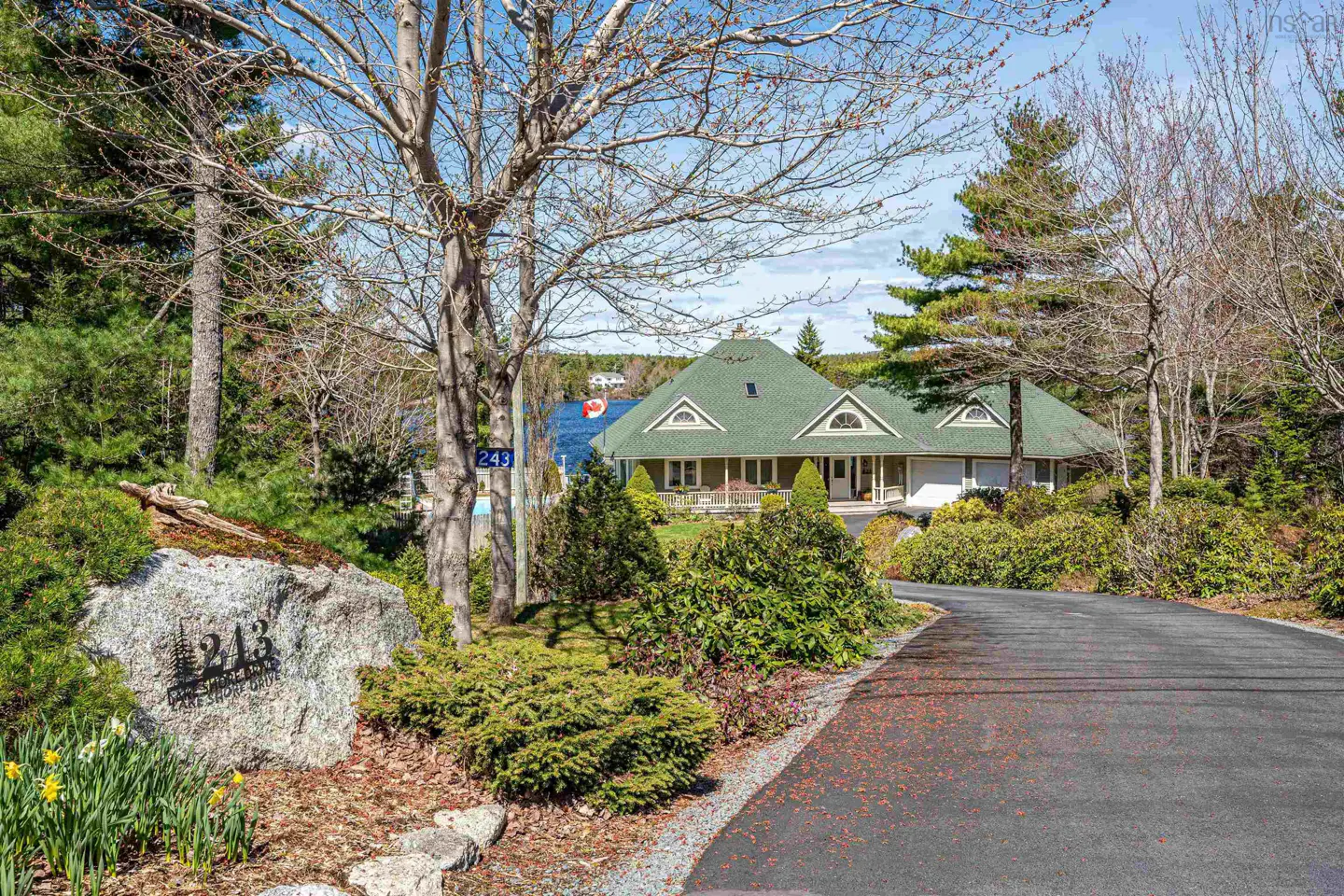 Exterior view of a house with a green roof, surrounded by trees and greenery, with a lake in the background.