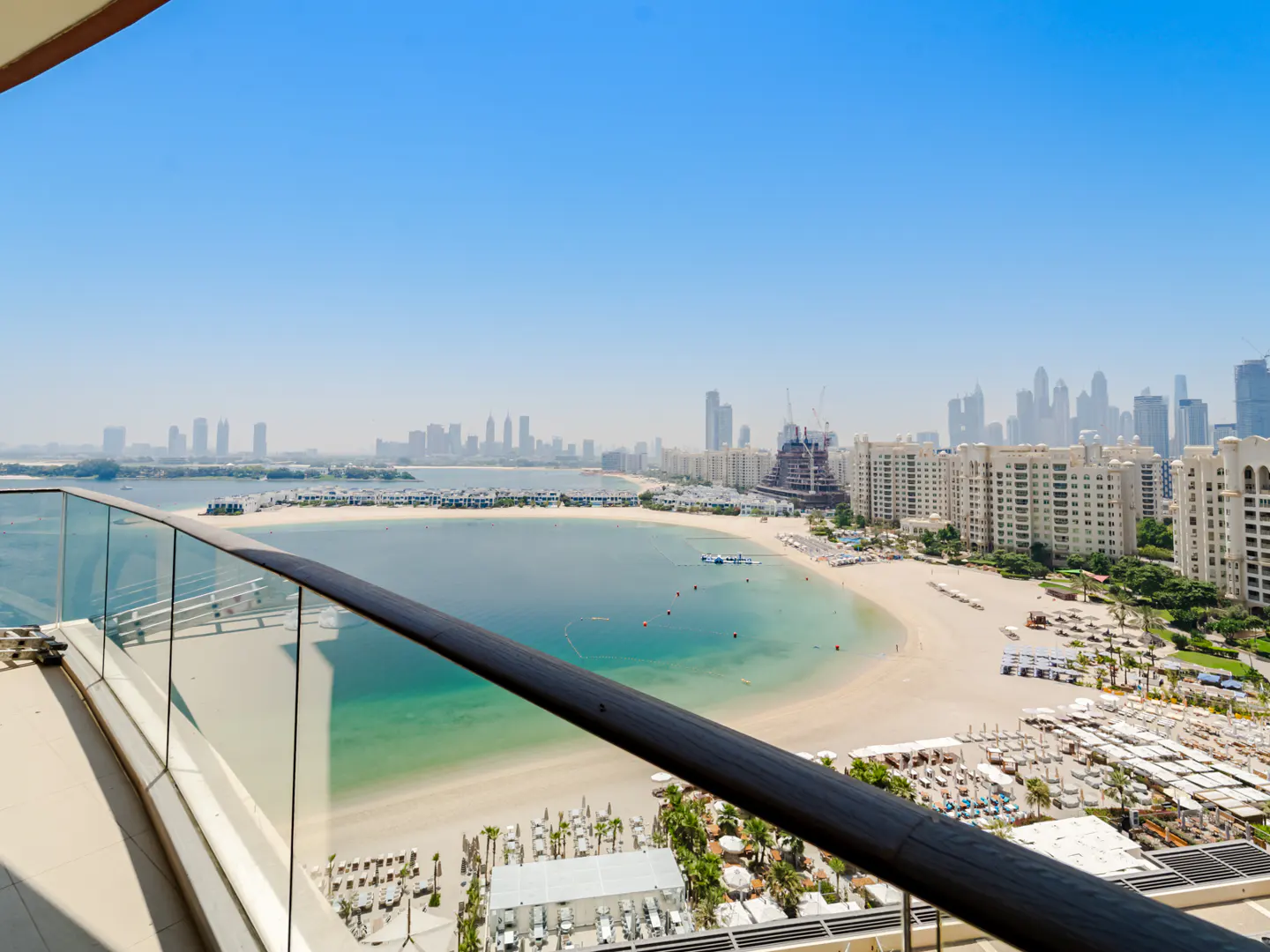 Balcony view of Dubai's Palm Jumeirah, featuring a beach, turquoise water, and city skyline under a clear blue sky.