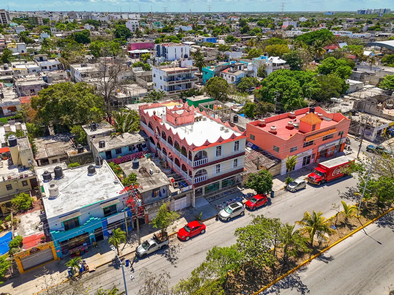 Aerial view of a neighborhood with colorful buildings, trees, cars, and a Coca-Cola truck on a sunny day.