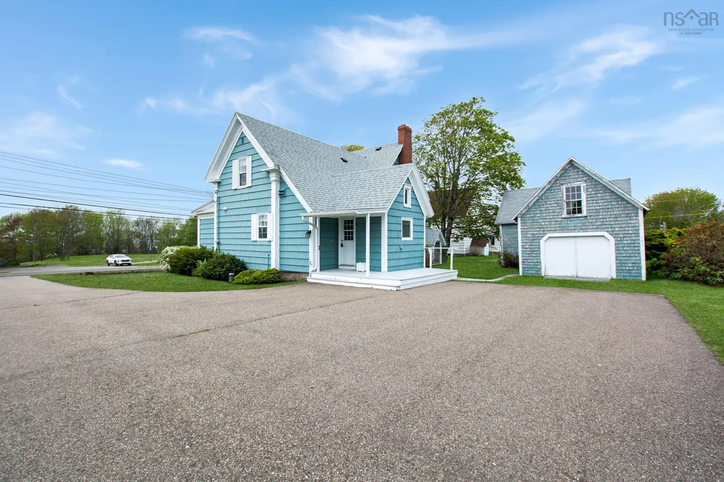 Exterior view of a light blue house with white trim, a gray roof, and a detached garage on a sunny day.