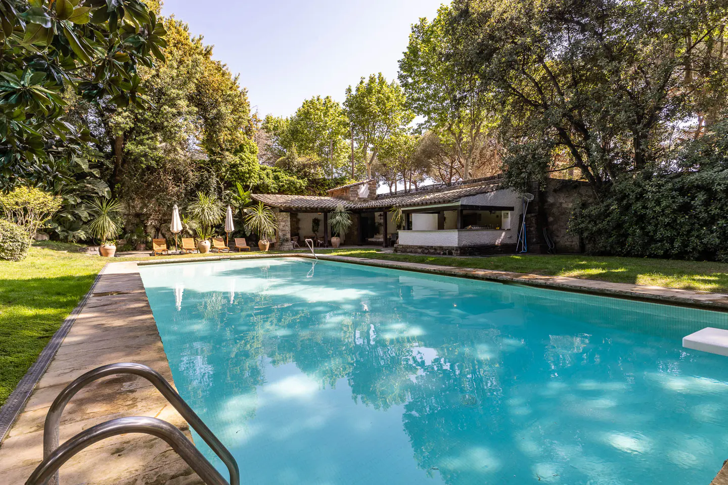 A turquoise swimming pool surrounded by trees, lounge chairs, and a pool house.