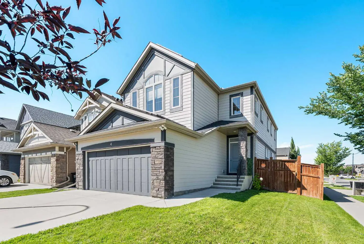 Two-story house with gray garage door, stone accents, and light siding under a blue sky. Green lawn and trees.