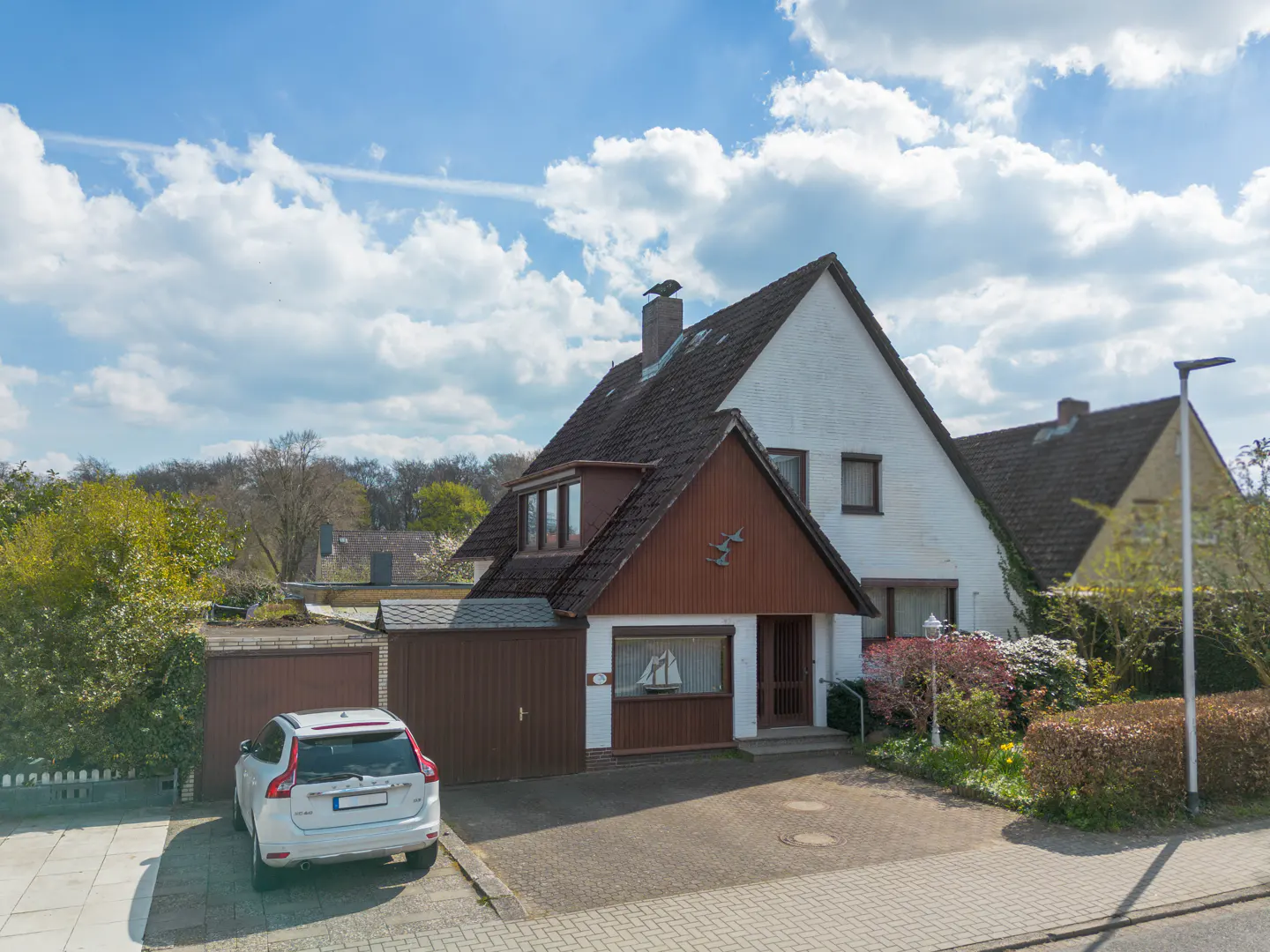 Two-story house with brown trim and a white car parked in front on a sunny day.