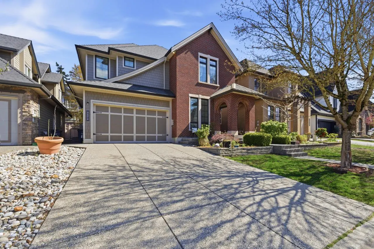 Two-story house with a brick facade, gray siding, and a gray garage door. A concrete driveway leads to the house.