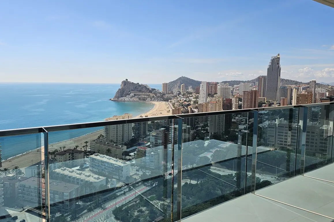 Balcony view of Benidorm, Spain. Blue sea, sandy beach, and city skyline with tall buildings under a clear sky.