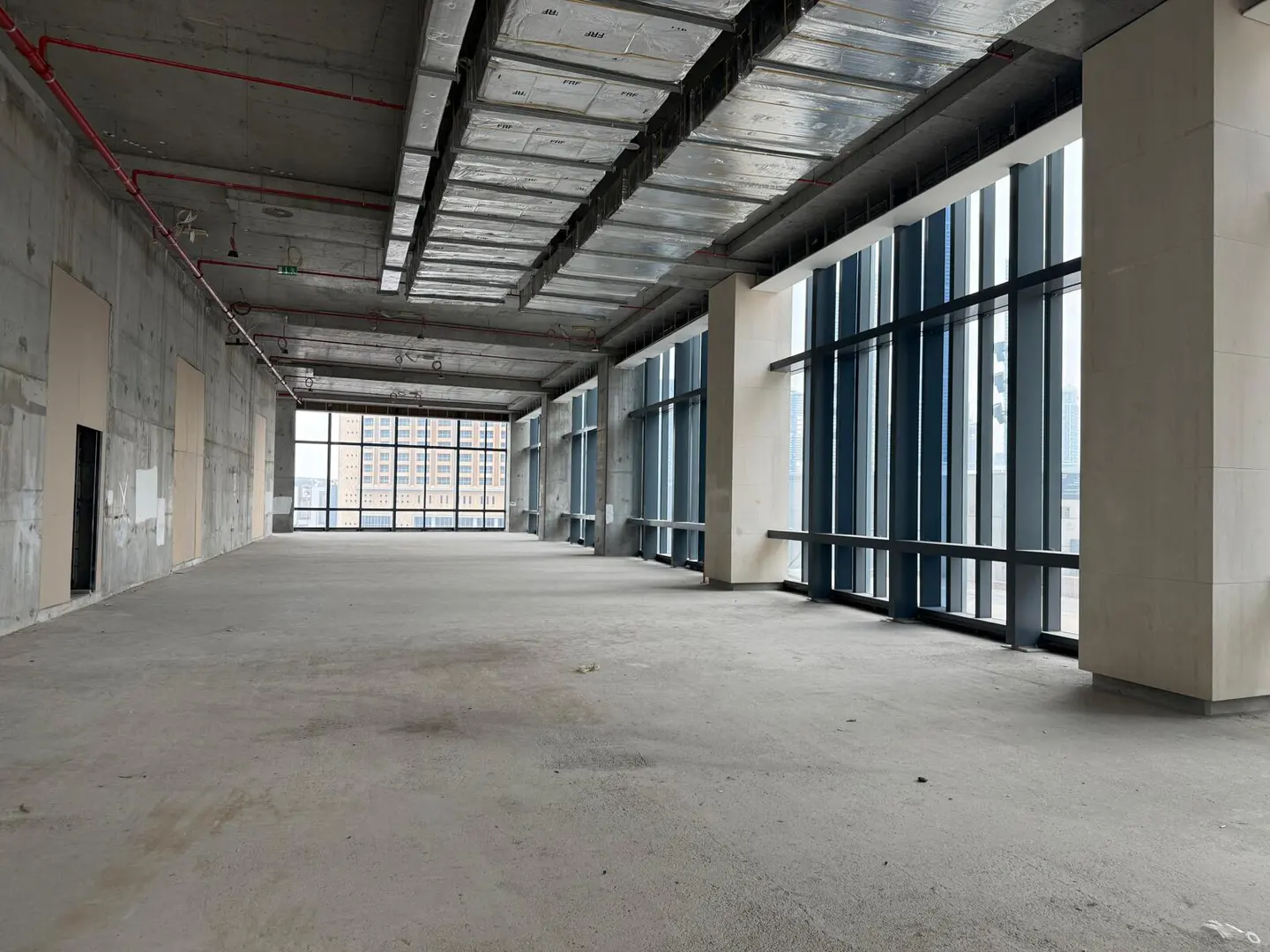 Unfinished office space with concrete floors, walls, and ceiling. Large windows with black frames offer a city view.