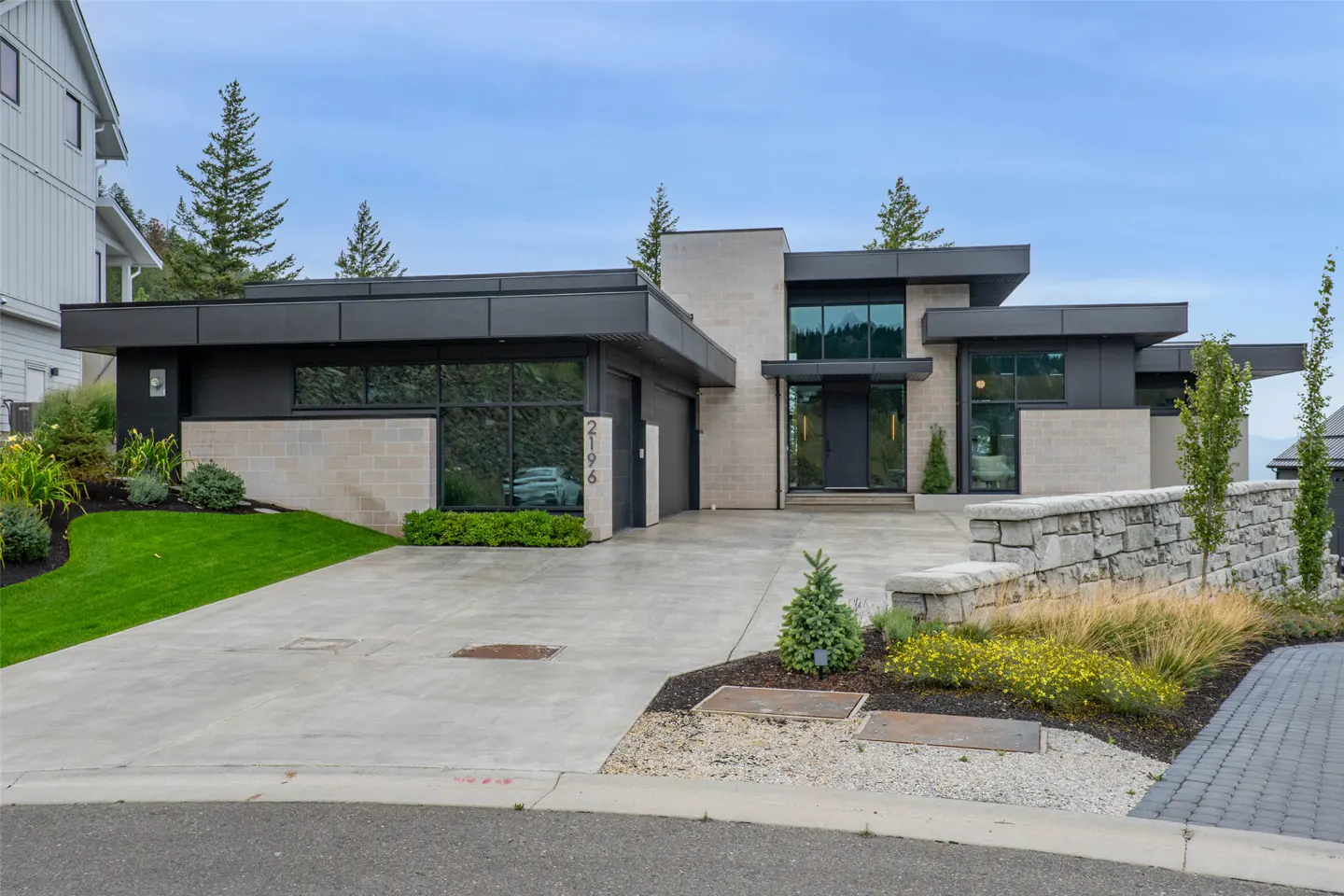 Modern single-story home with black metal accents, stone walls, a concrete driveway, and landscaped front yard.