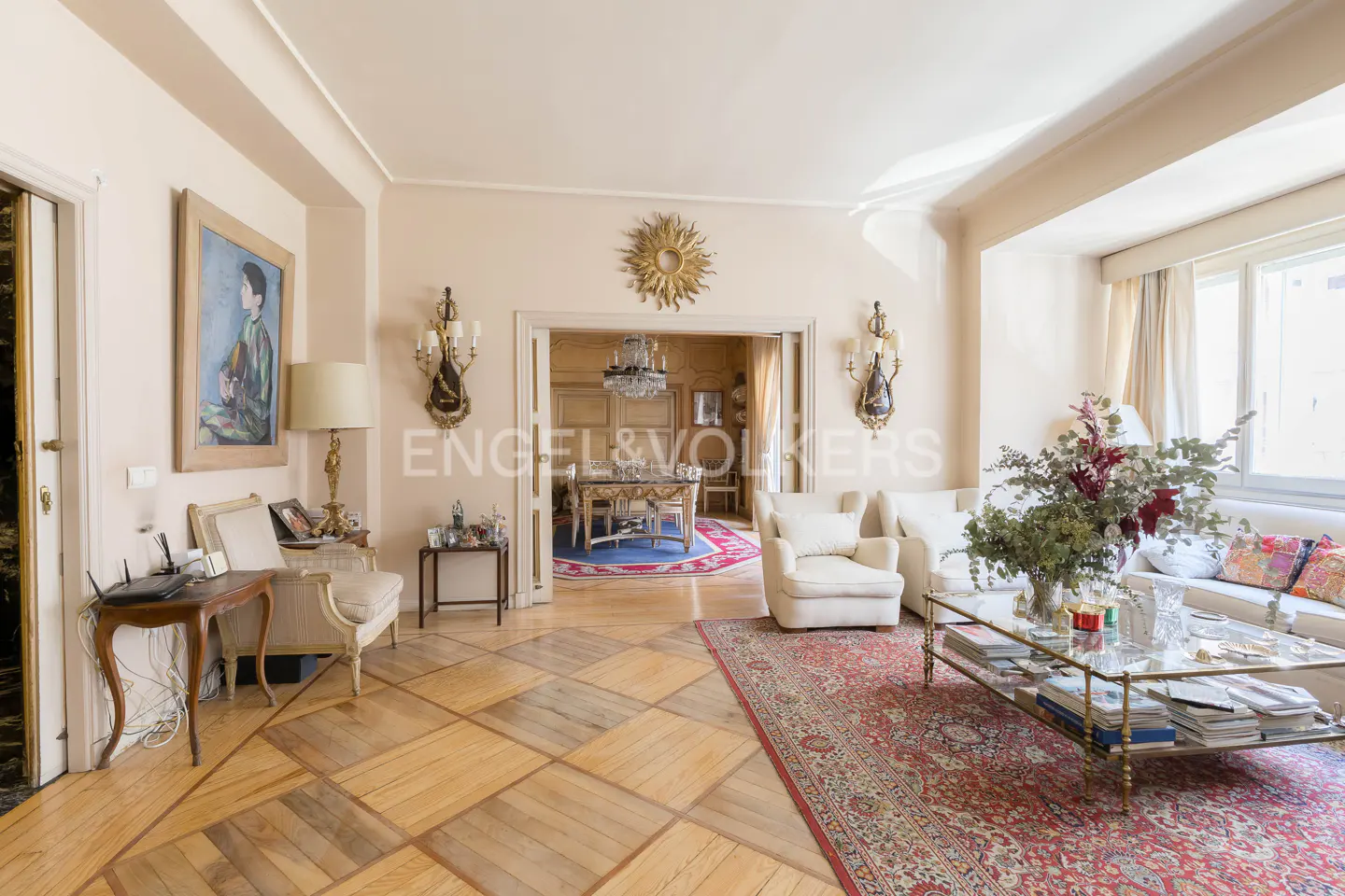A bright living room with a patterned wood floor, white sofas, and a dining room visible through an archway.