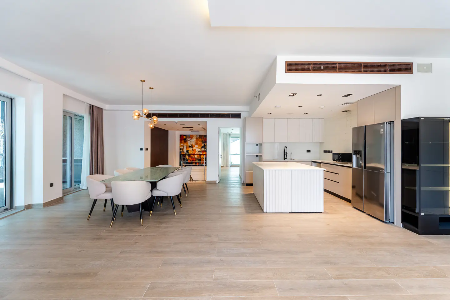 Open-concept living space with a dining table, chairs, and a modern white kitchen with stainless steel appliances.