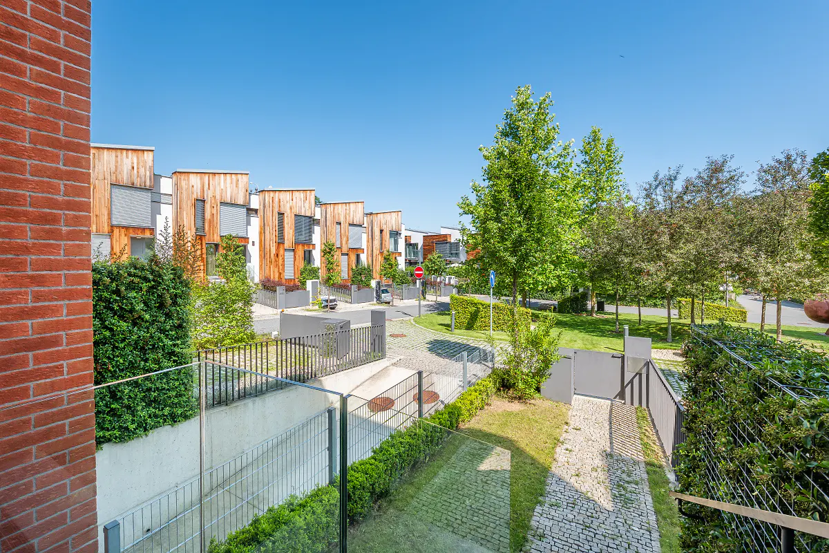 View of modern townhouses with wood facades, green lawns, and a clear blue sky. Brick wall in foreground.