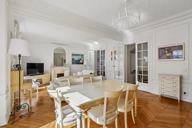 Bright living and dining room with white walls, herringbone wood floors, a dining set, and a fireplace with a mirror.