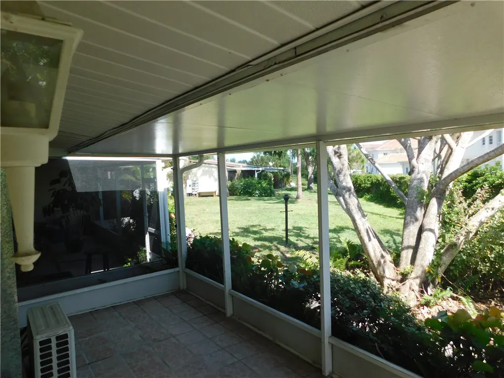 Screened-in porch with tile floor and white frame, overlooking a green lawn with trees and shrubs.