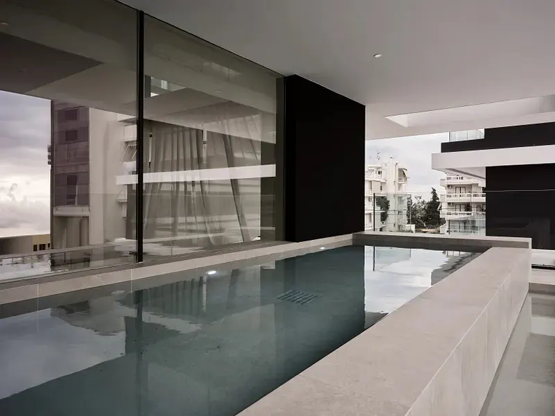 Rooftop pool with city view. The pool's water reflects the sky. Modern architecture with glass walls and black accents.