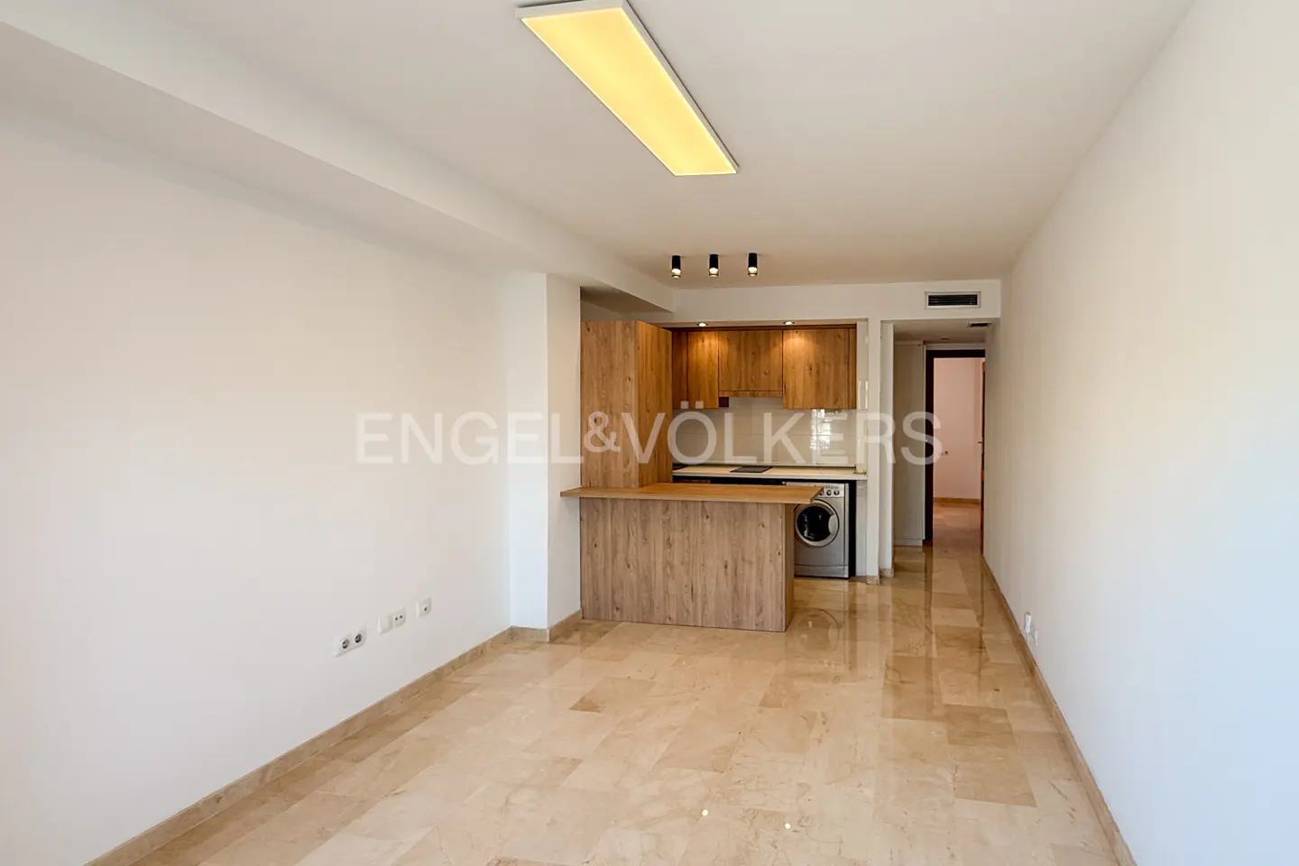 A bright, empty room with marble floors and a wood kitchen with a breakfast bar.