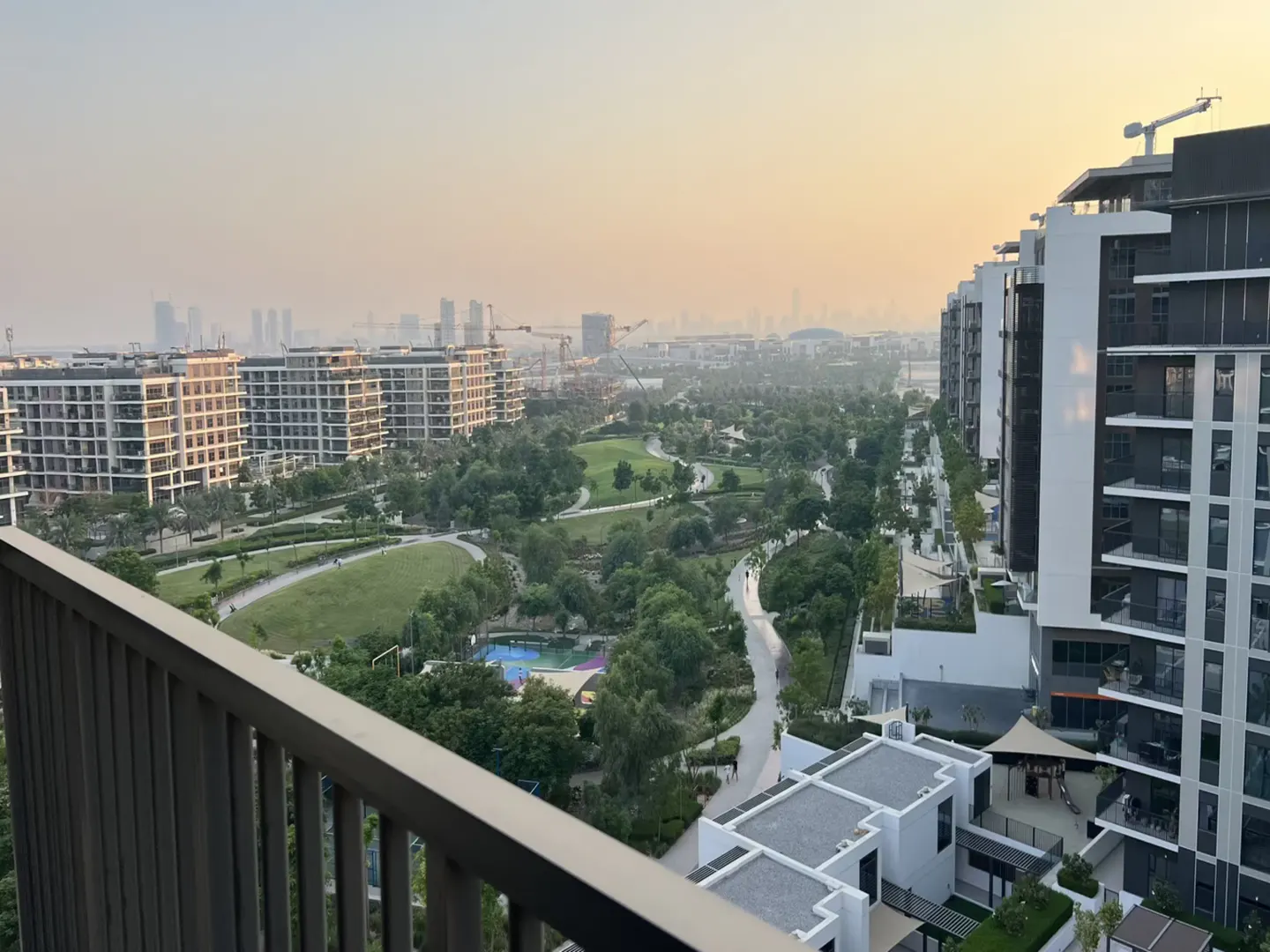 High-angle view of modern apartment buildings overlooking a lush green park with walking paths at sunset.