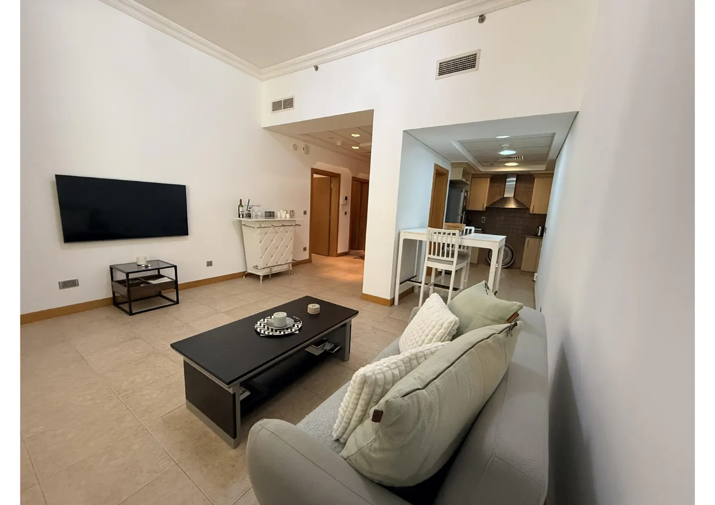 Living room with a gray sofa, black coffee table, and TV. A kitchen is visible in the background.