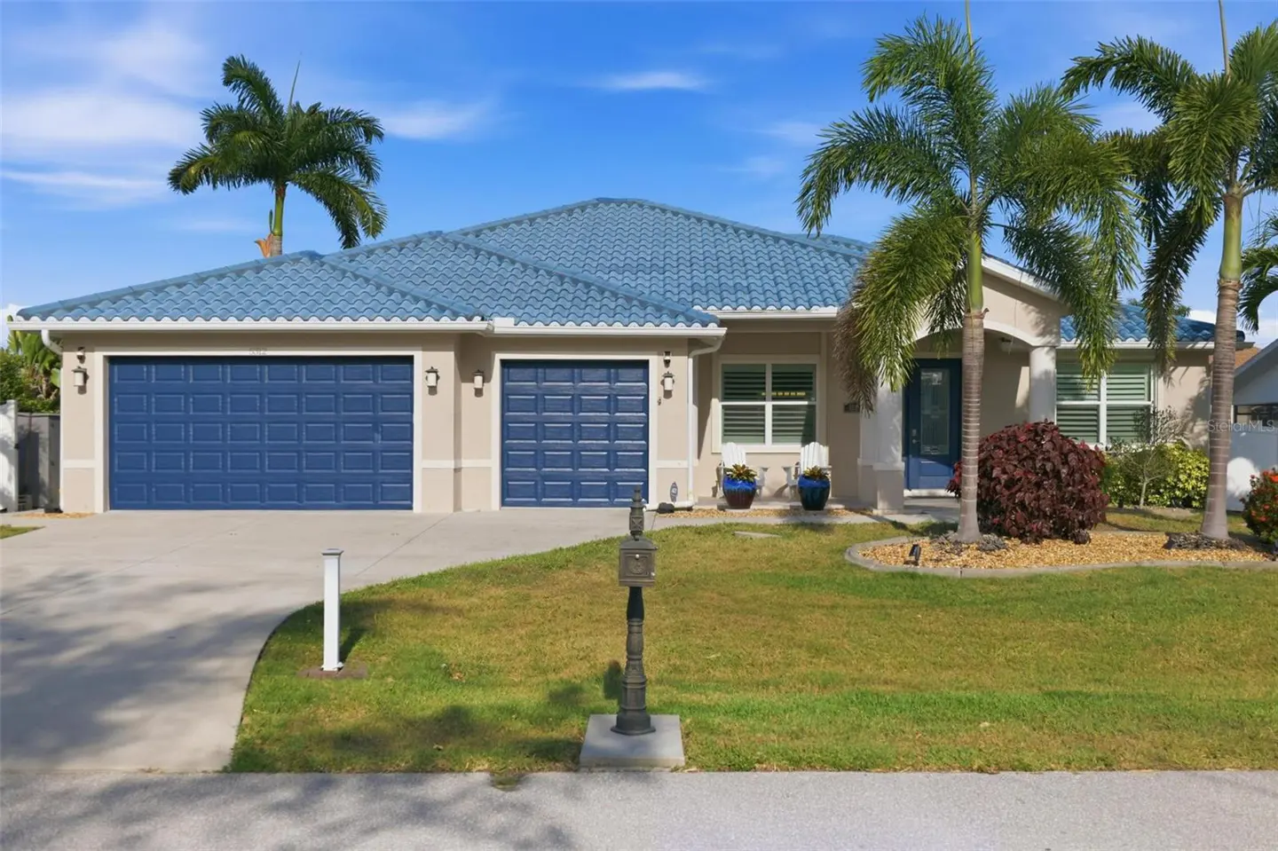 Beige single-story house with a blue tile roof, blue garage doors, and palm trees in the front yard.