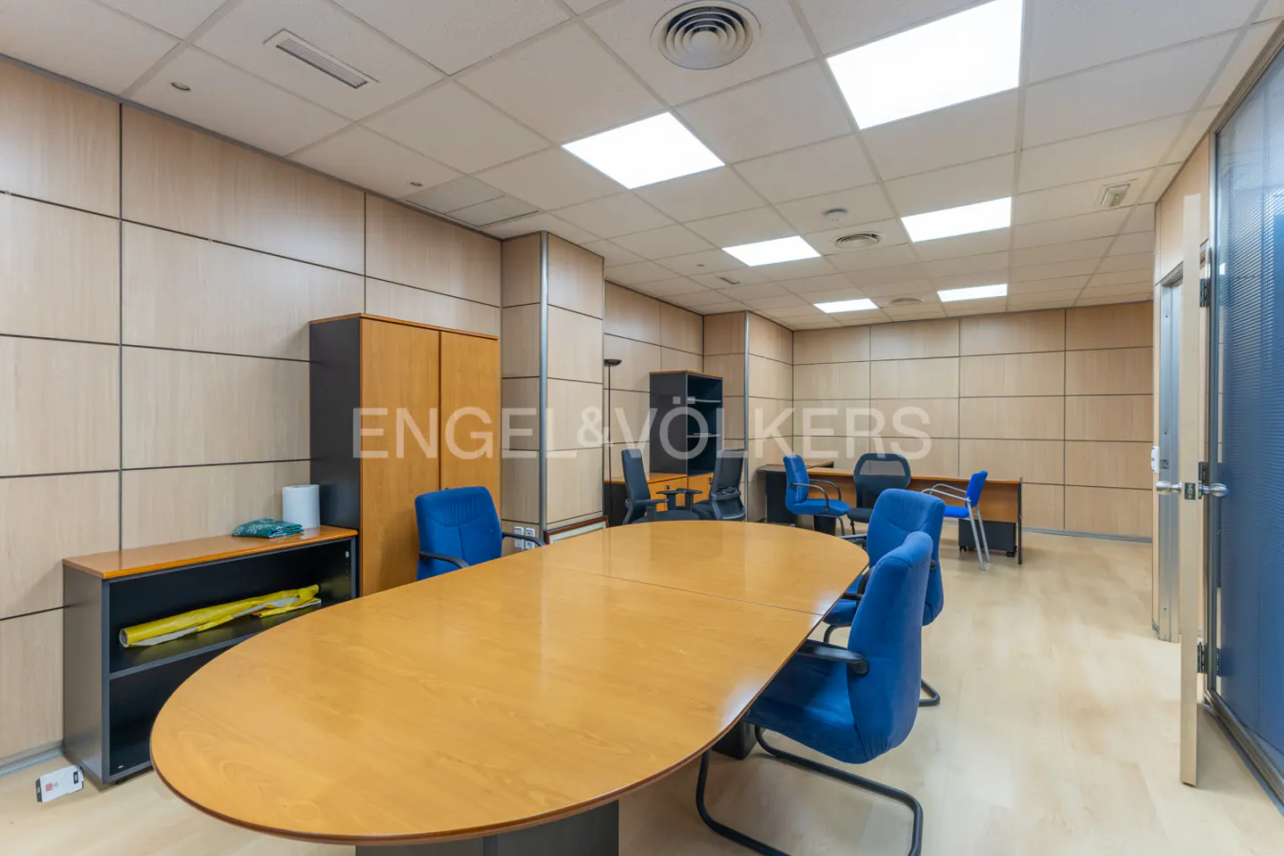 Bright office space with a large wooden conference table and blue chairs, desks, and cabinets.