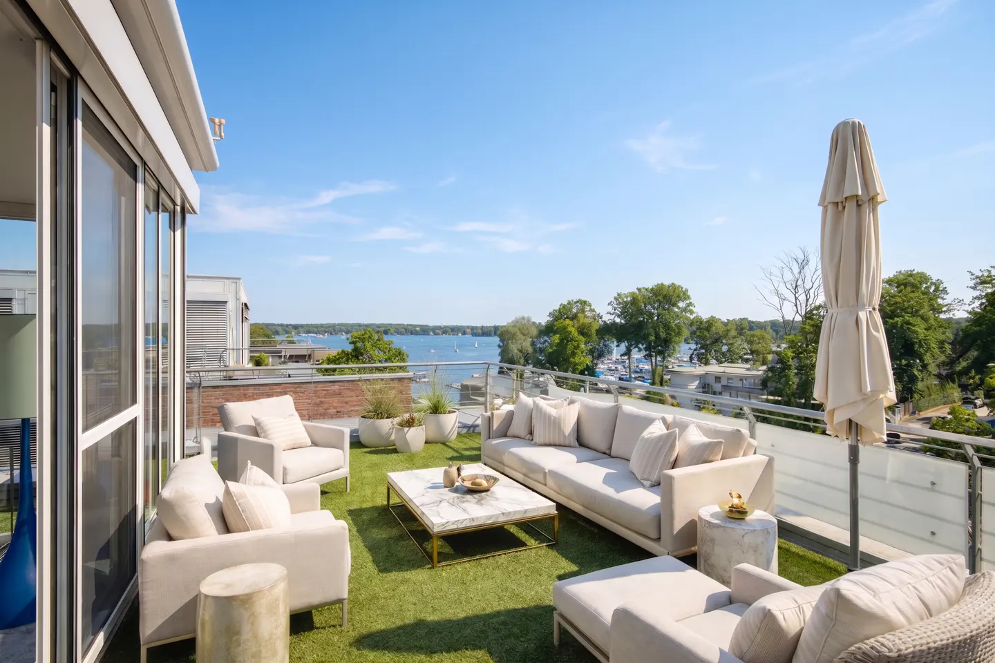 Rooftop patio with white furniture, green turf, and a view of a lake and trees under a blue sky.