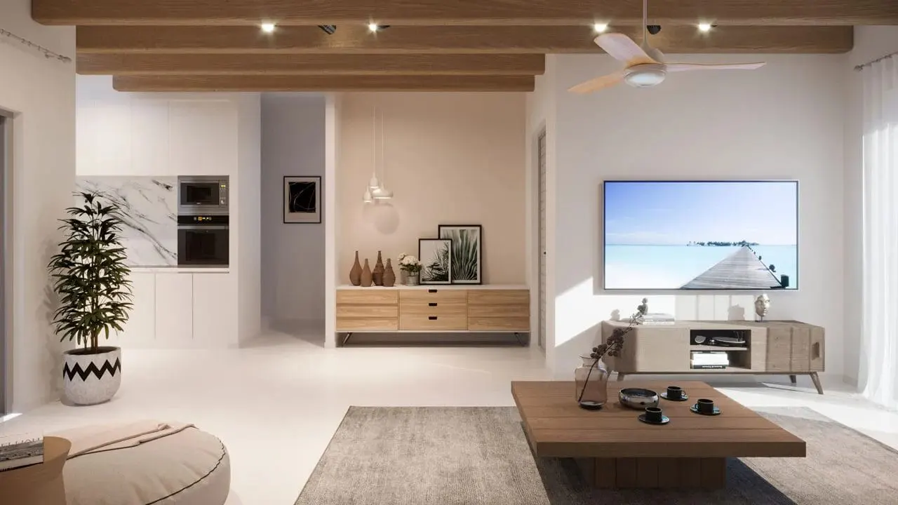 Bright living room with wood beams, fan, TV, and furniture. Kitchen area visible in the background.