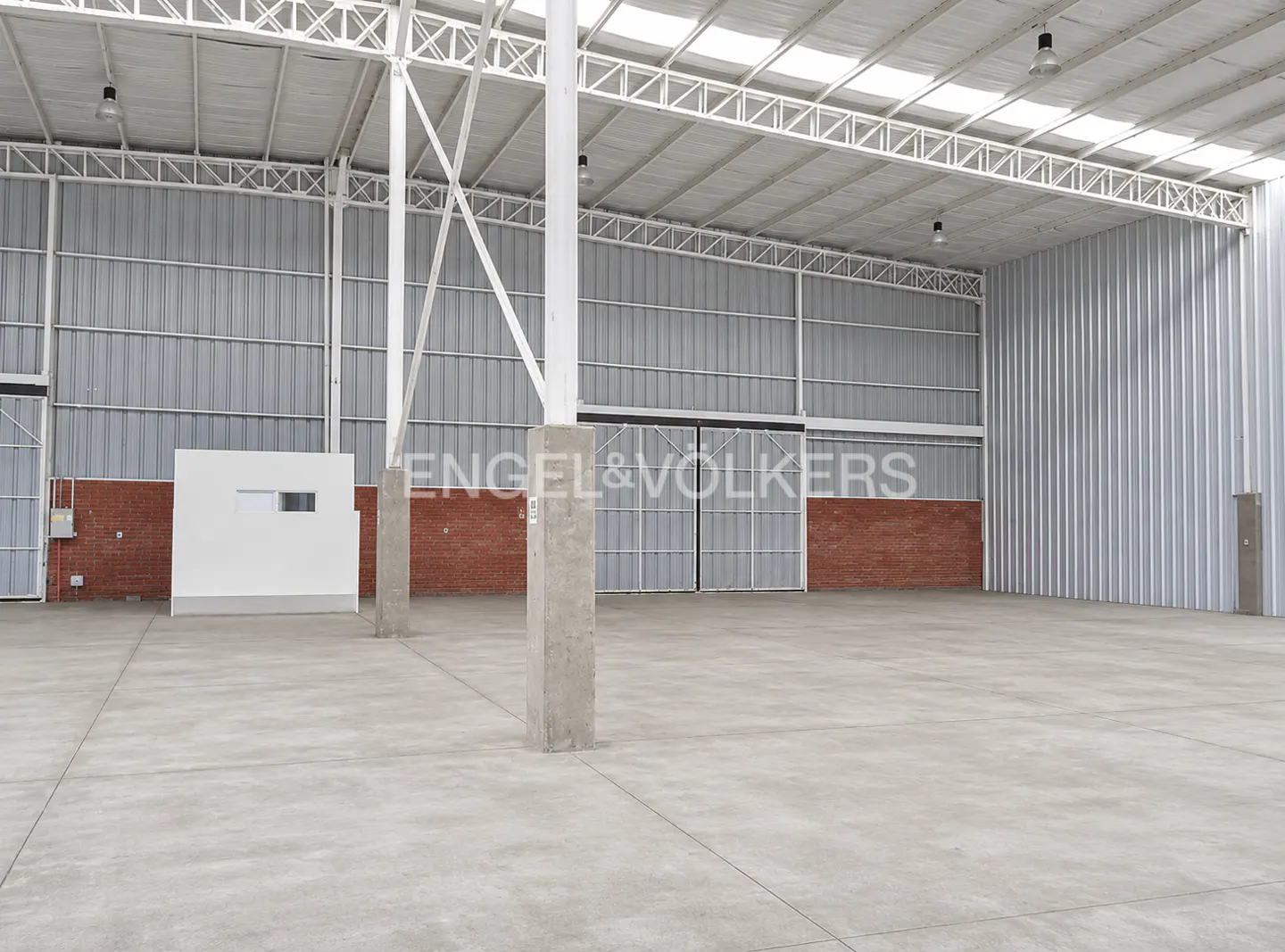An empty warehouse with a concrete floor, metal walls, and a white ceiling with metal beams.